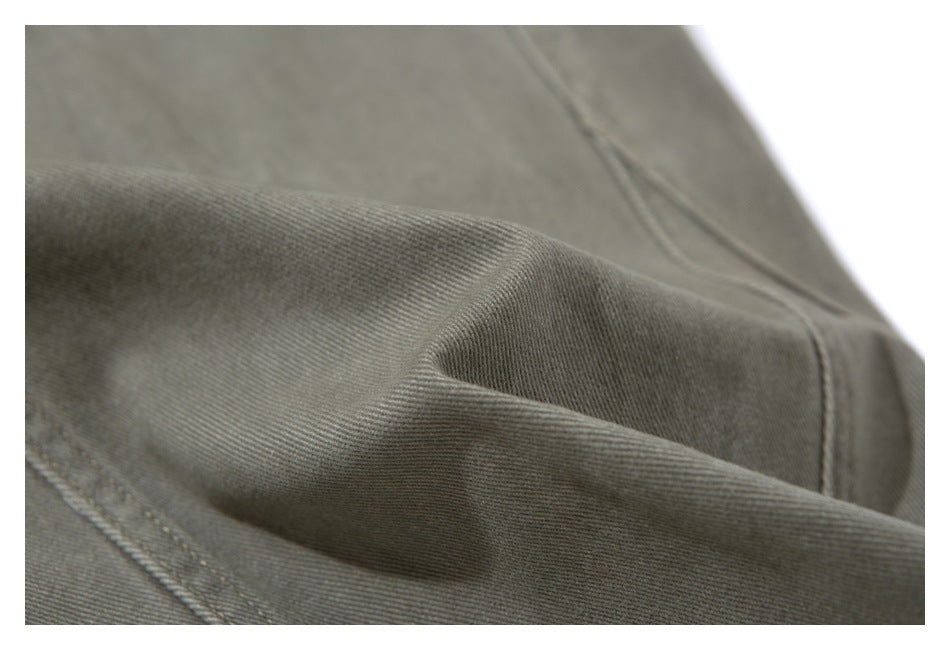 Macro view of olive-gray pants fabric, folded to show its fine diagonal weave and stitching.