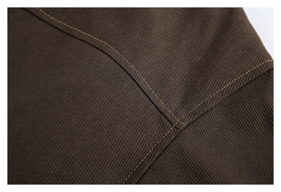 Close-up of dark brown ribbed fabric with curved seams and tan stitching.