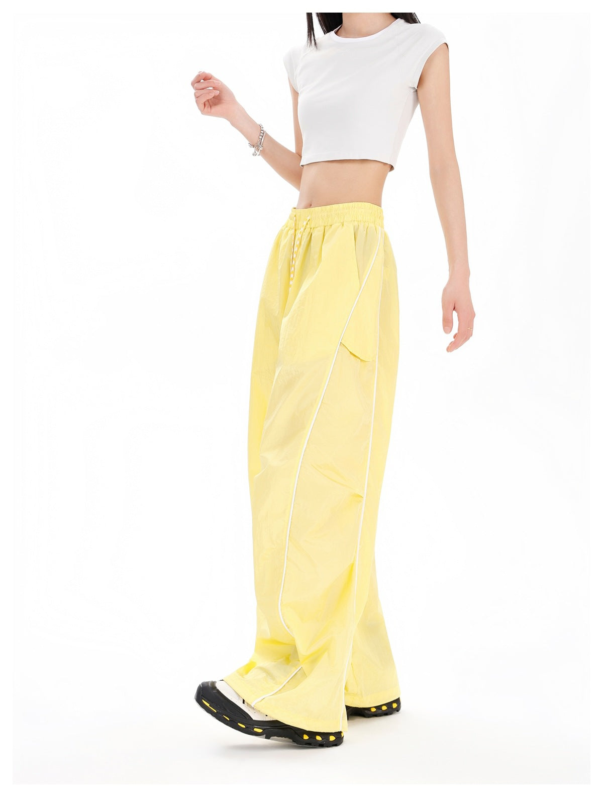 Model in yellow wide-leg pants with white side piping and a thigh flap pocket, shown at a three-quarter angle