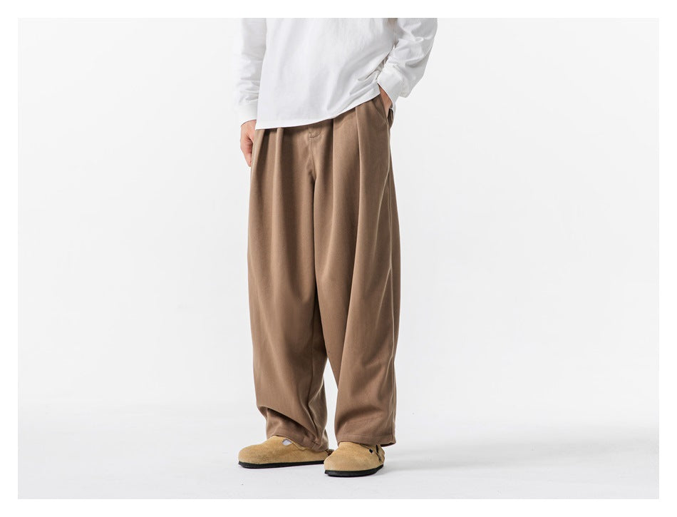 Front three-quarter view of a person wearing loose brown trousers and a white long-sleeve shirt.