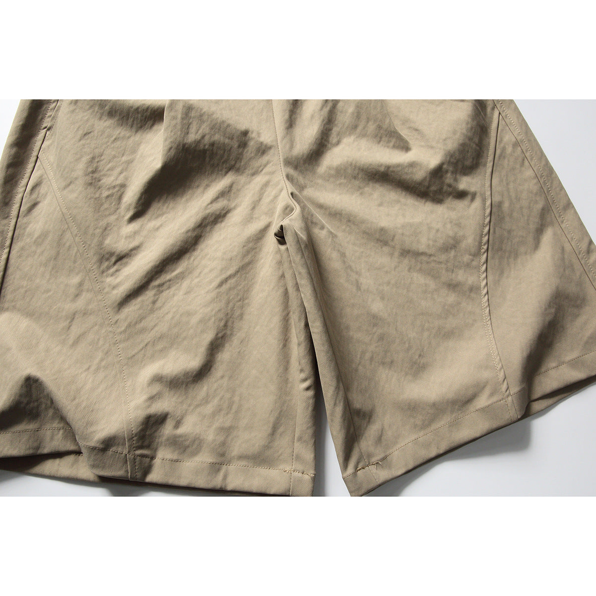 Close-up of beige shorts showing the front crotch seam, leg panels, and stitched hems.