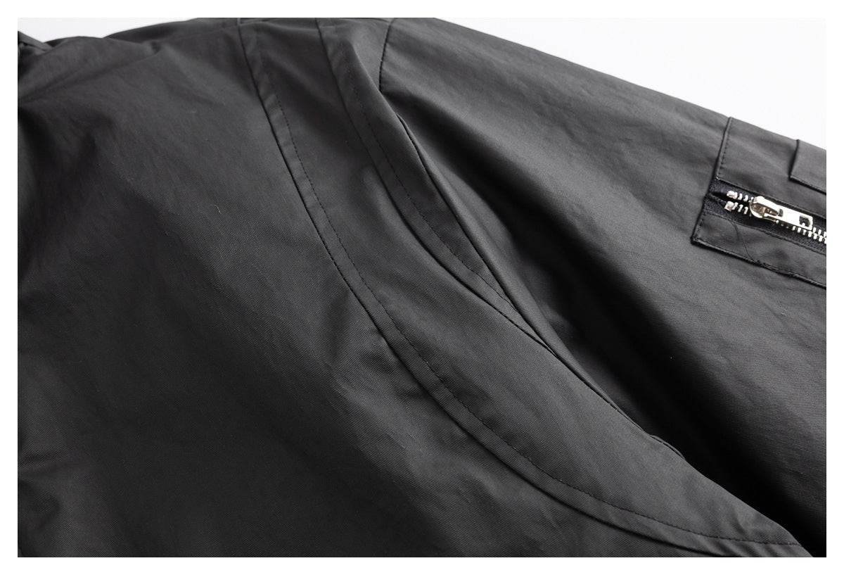 Black garment close-up showing a curved stitched pocket opening and a small silver zipper.