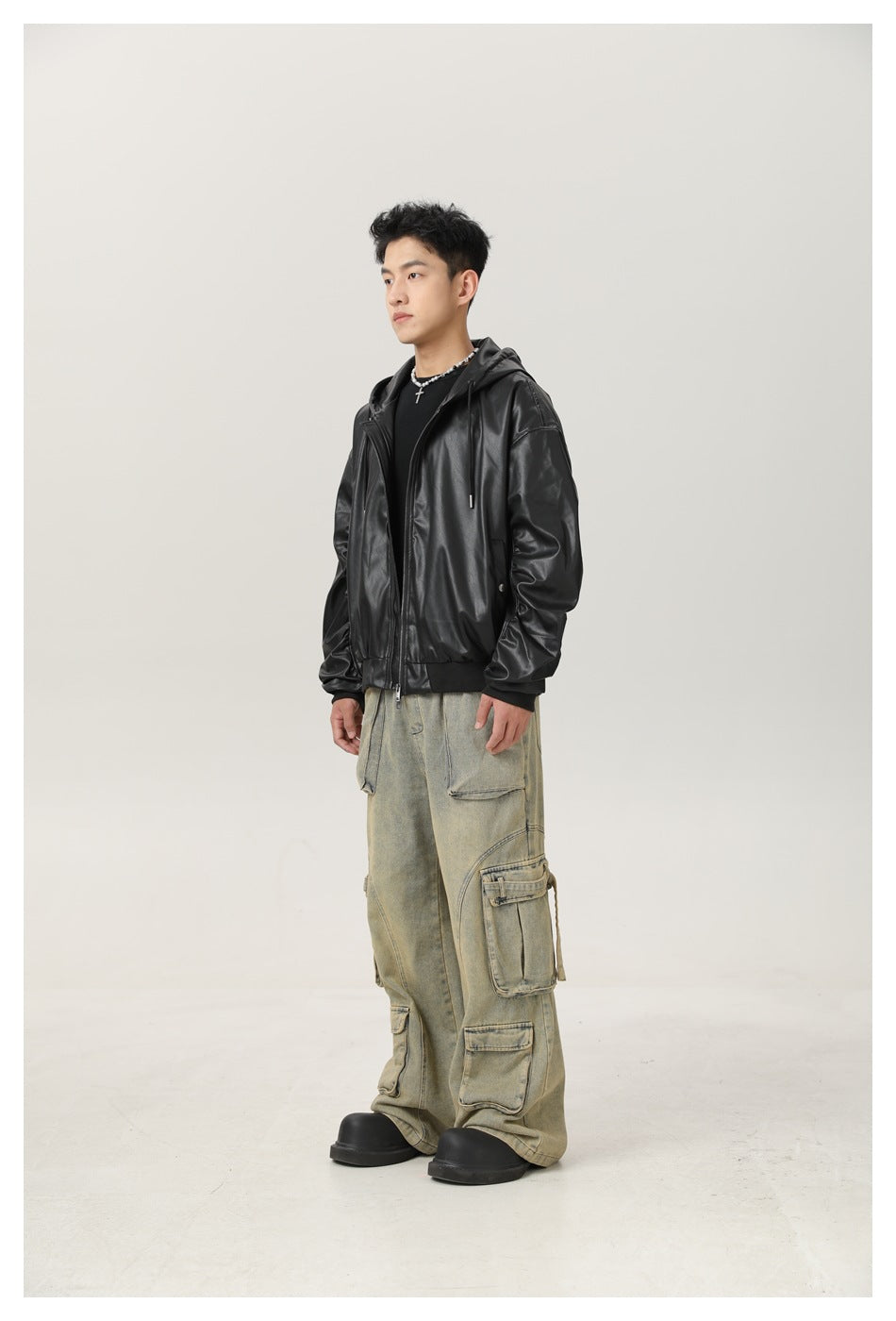 Model wearing black faux-leather hooded zip jacket over a black top with wide-leg cargo jeans, side view
