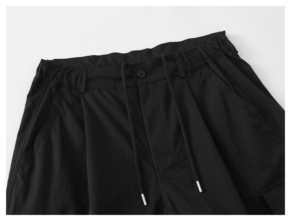 Close-up of black pants showing the gathered drawstring waistband, button closure, and front pleats.