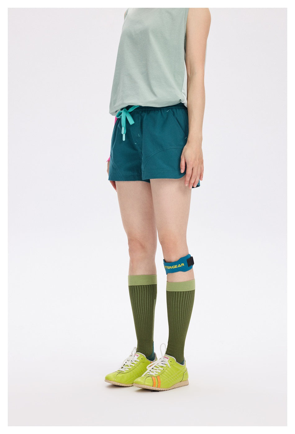 Front view of a model wearing teal running shorts with a turquoise drawstring and curved front pockets.