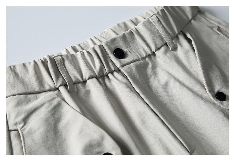 Close-up of light gray trousers showing an elastic waistband, belt loops, pockets, and black buttons.