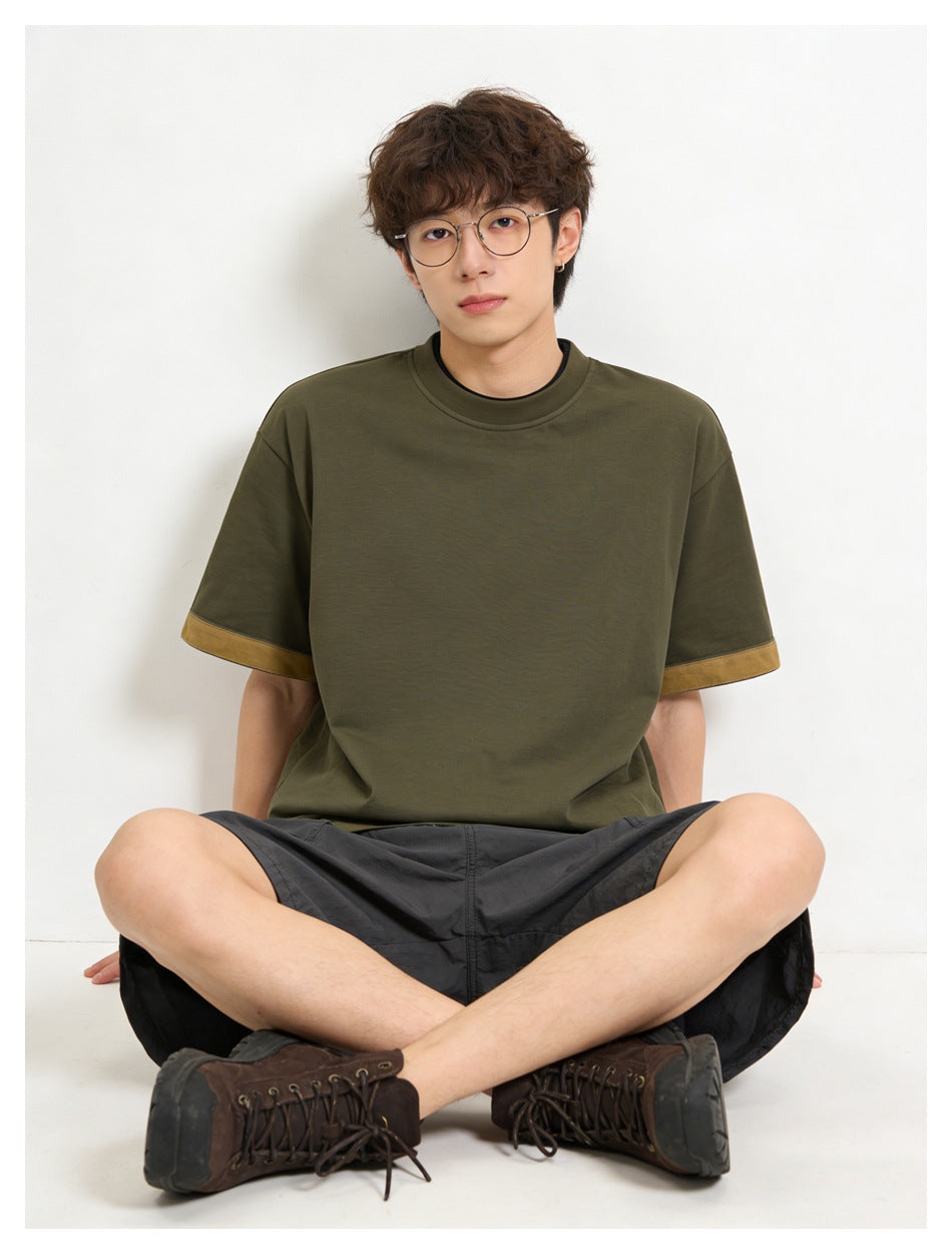 Seated model wearing an olive T-shirt with mustard sleeve cuffs and charcoal shorts.