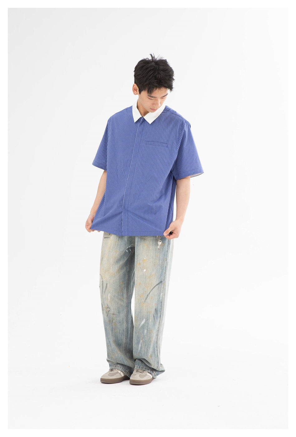 Model wearing blue striped short-sleeve collared shirt with distressed jeans, looking down and holding the hem
