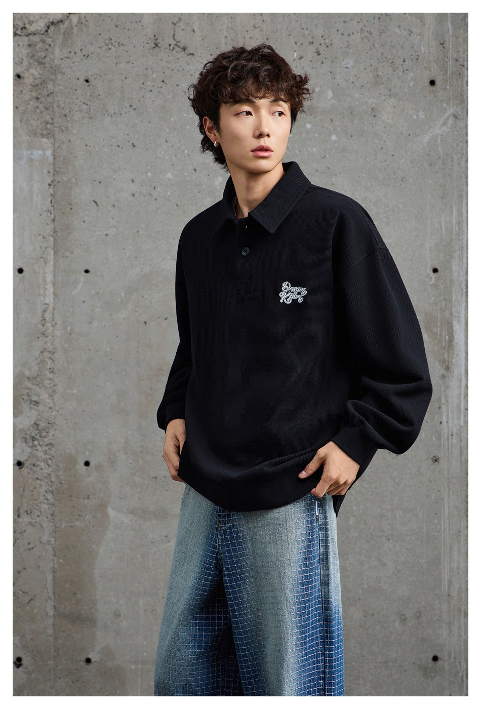 Model in a black oversized collared pullover with white chest embroidery, shown from a slight angle.