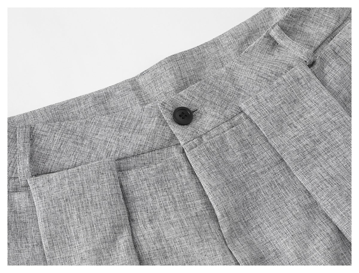 Close-up of light gray trousers showing the waistband, black button, fly, and slanted front pocket.