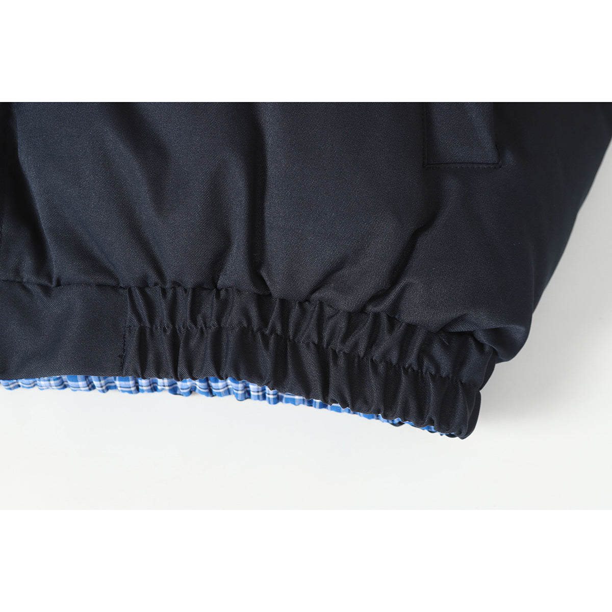 Close-up of the dark navy jacket's gathered hem with blue plaid lining visible underneath.