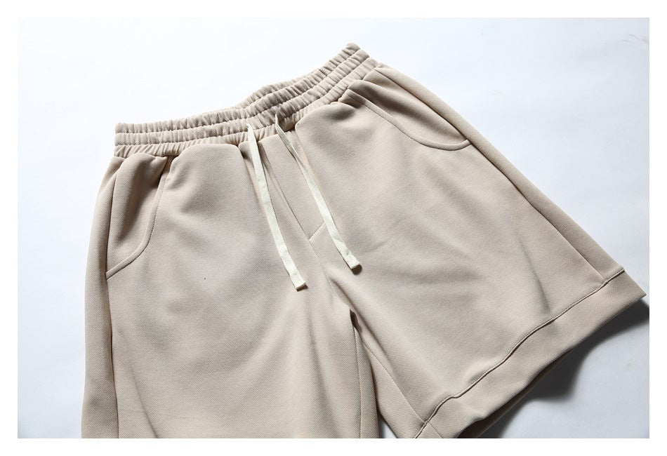 Beige shorts laid flat, showing an elastic waistband, cream drawstrings, curved pockets and wide hems.