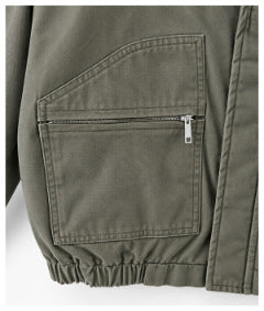 Close-up of the olive-gray jacket's large front pocket with a horizontal zipper and elasticized hem.