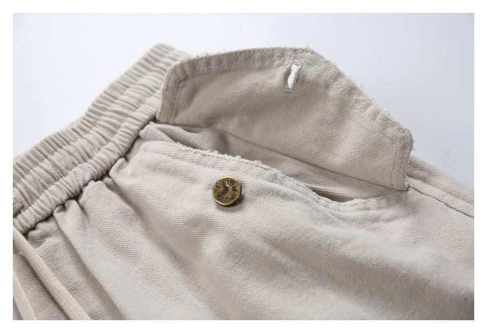 Close-up of a beige flap pocket lifted to show its brass-tone button and stitching.