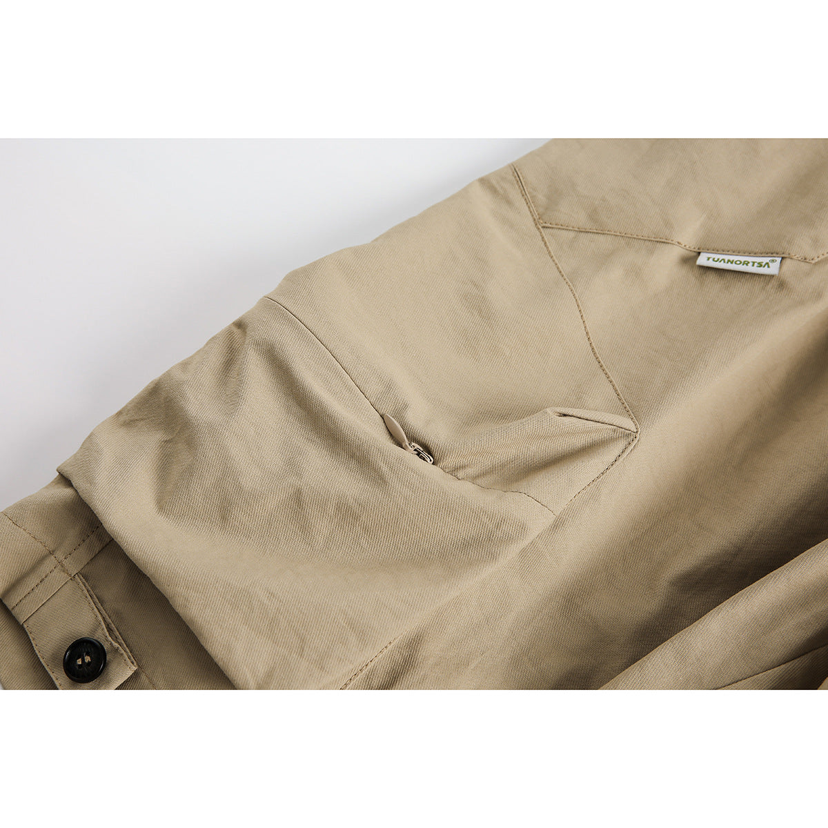 Close-up of tan shorts showing a zip pocket, seams, button, and small sewn-in label.