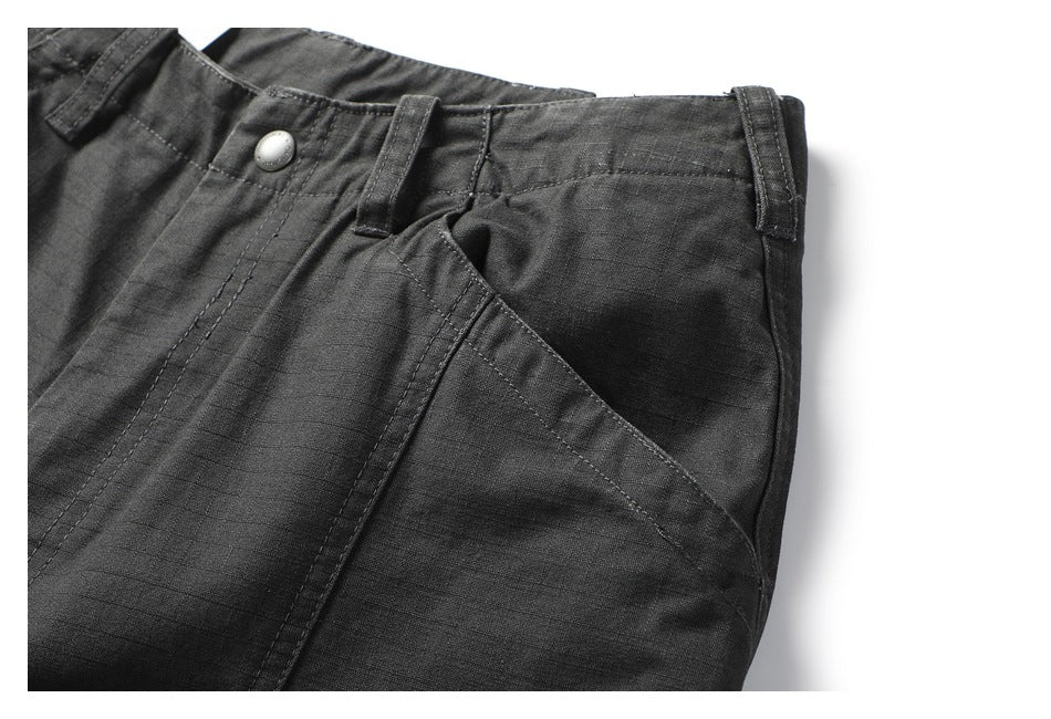 Close-up of charcoal trousers showing the waistband, belt loops, button, and slanted front pocket.