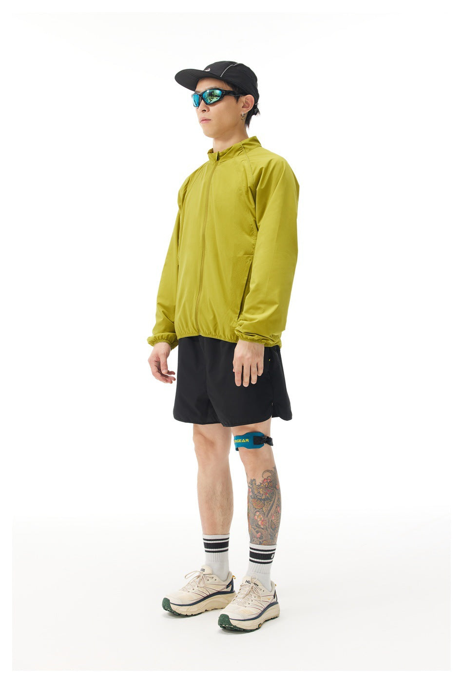 Side view of a man wearing a yellow-green zip-up jacket with black shorts and cap
