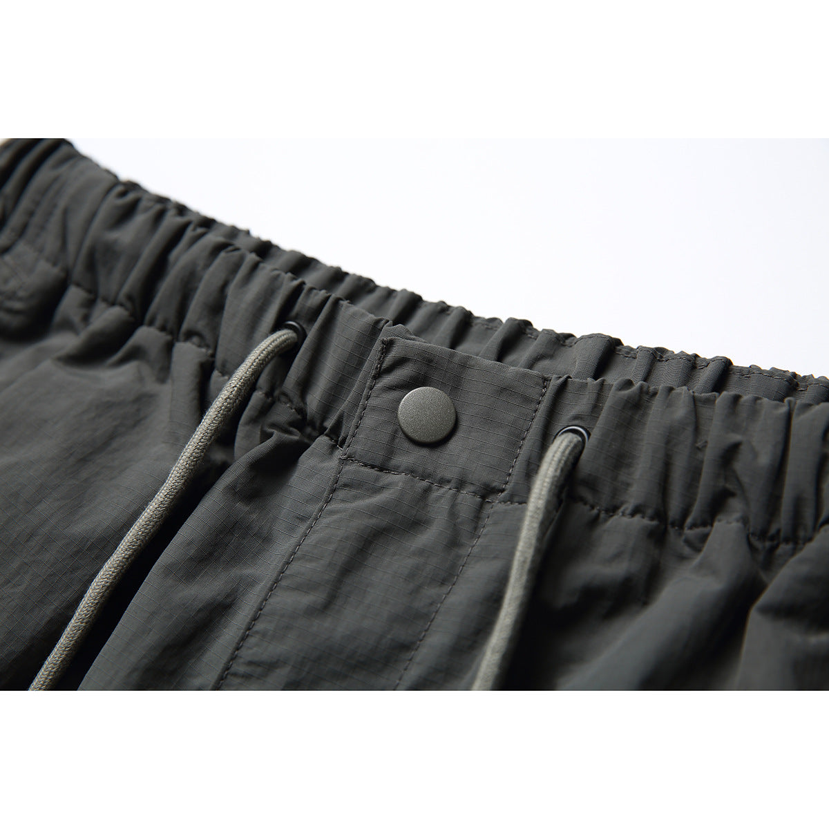 Close-up of dark charcoal pants showing an elastic drawstring waistband and a snap-button flap.