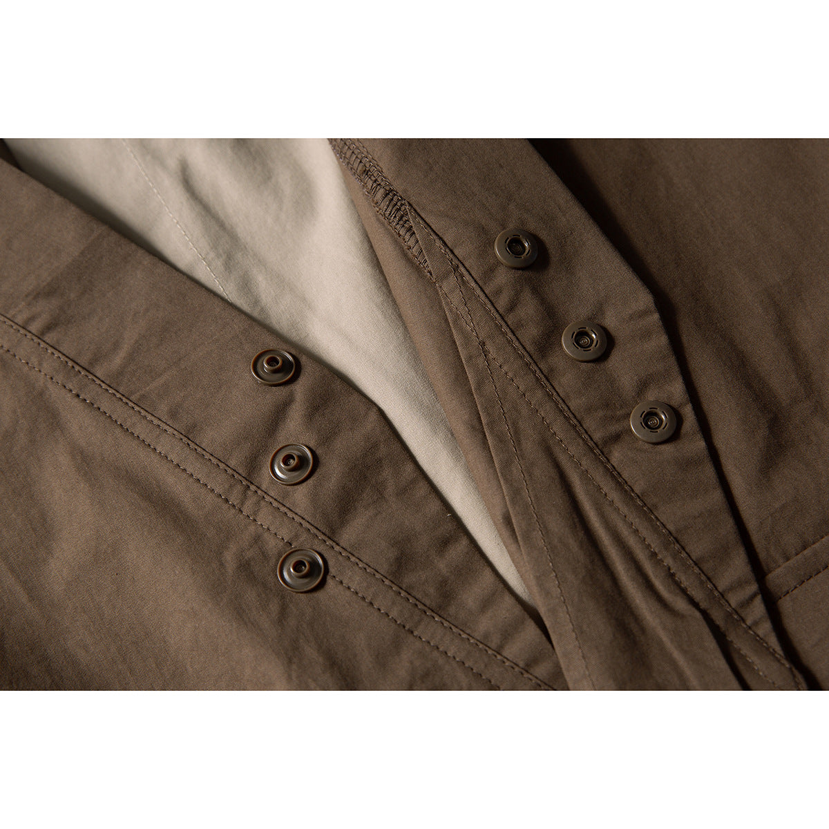 Close-up of snap fasteners and stitching on the brown vest over a beige shirt.
