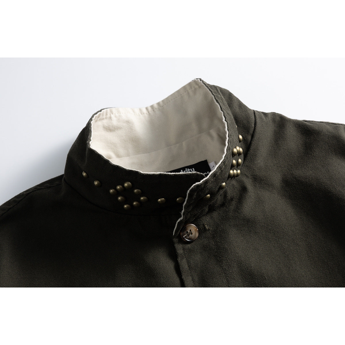 Close-up of an olive jacket's high collar with brass studs, pale lining, and a buttoned placket.