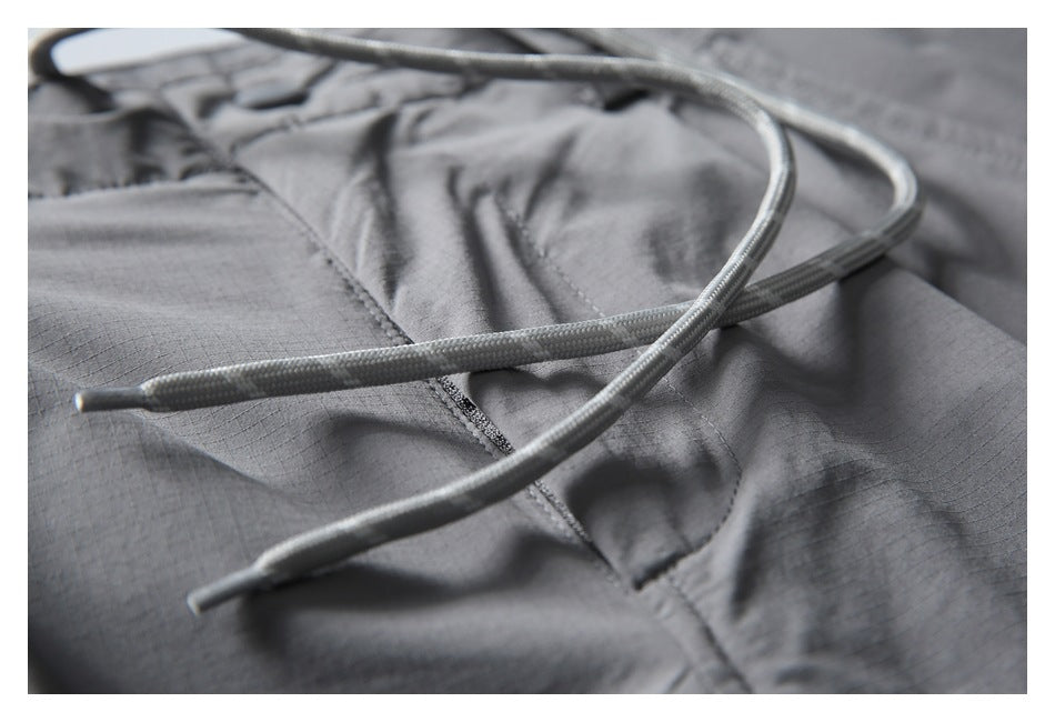 Close-up of white braided drawcords crossing the gray pants fabric beside a stitched pocket.