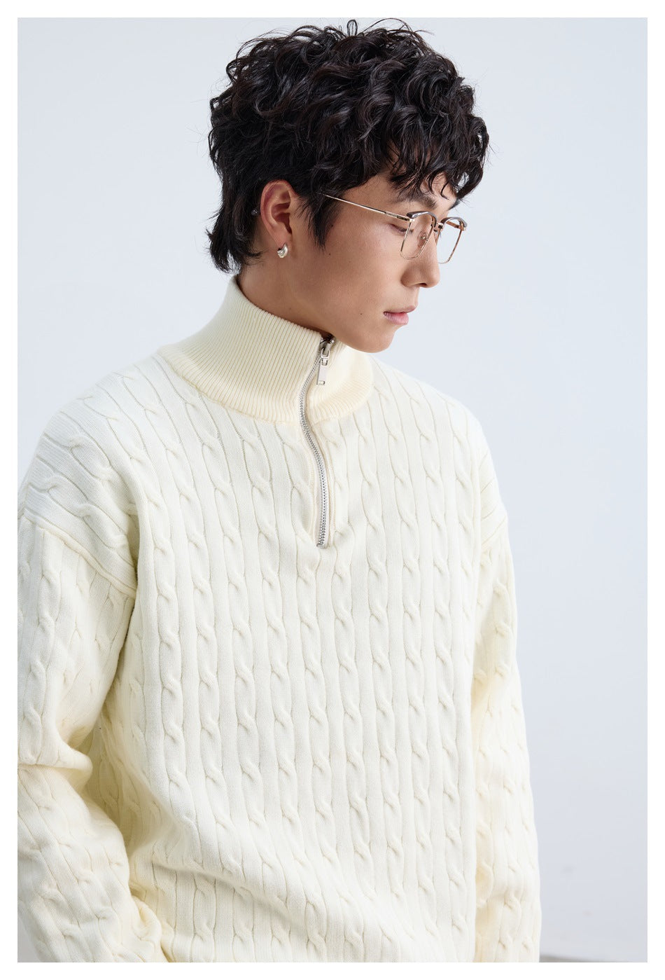 Close-up of an ivory cable-knit sweater showing its raised ribbed collar and silver quarter zipper.