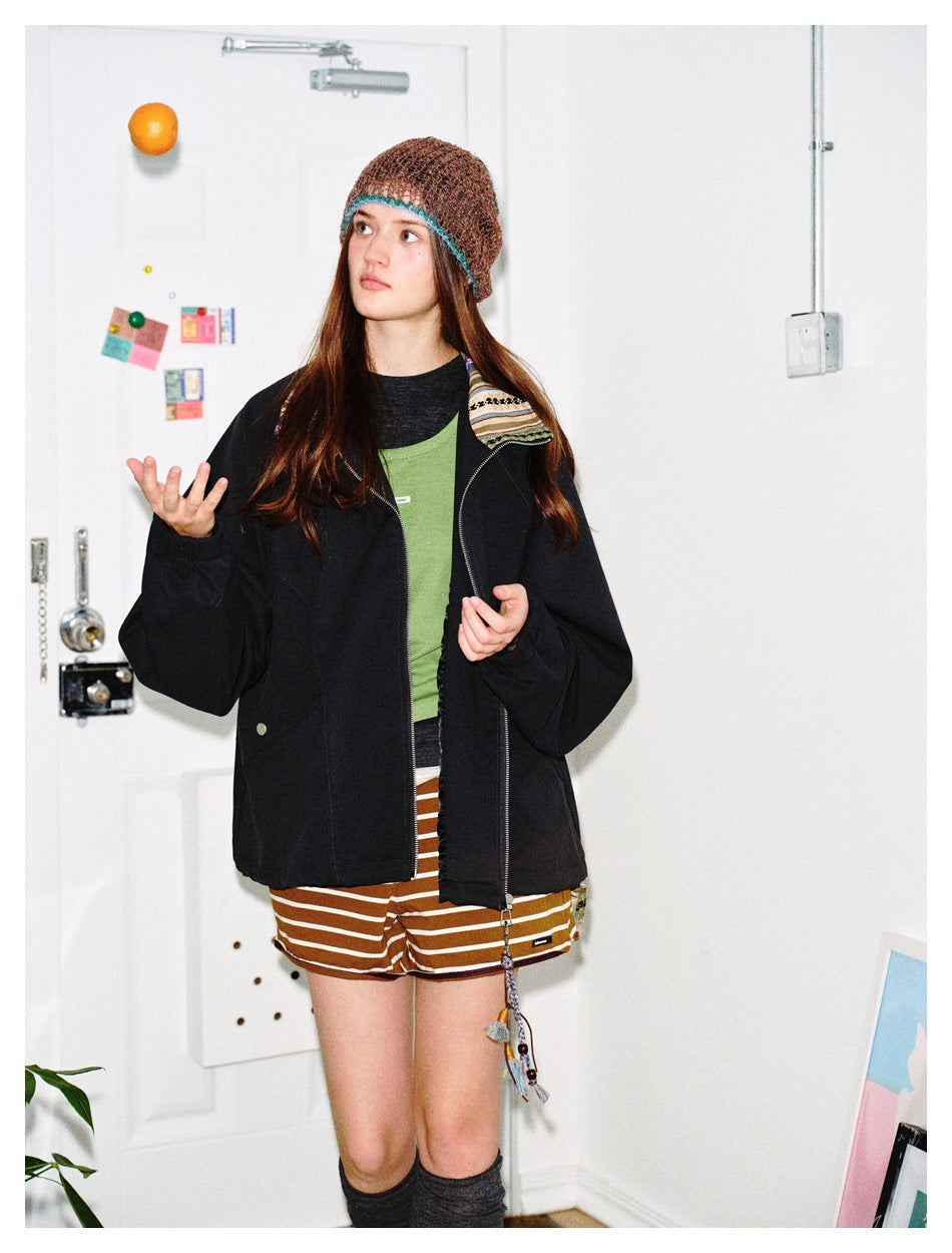 Model wearing an open black zip jacket with striped collar trim over a green top and striped shorts