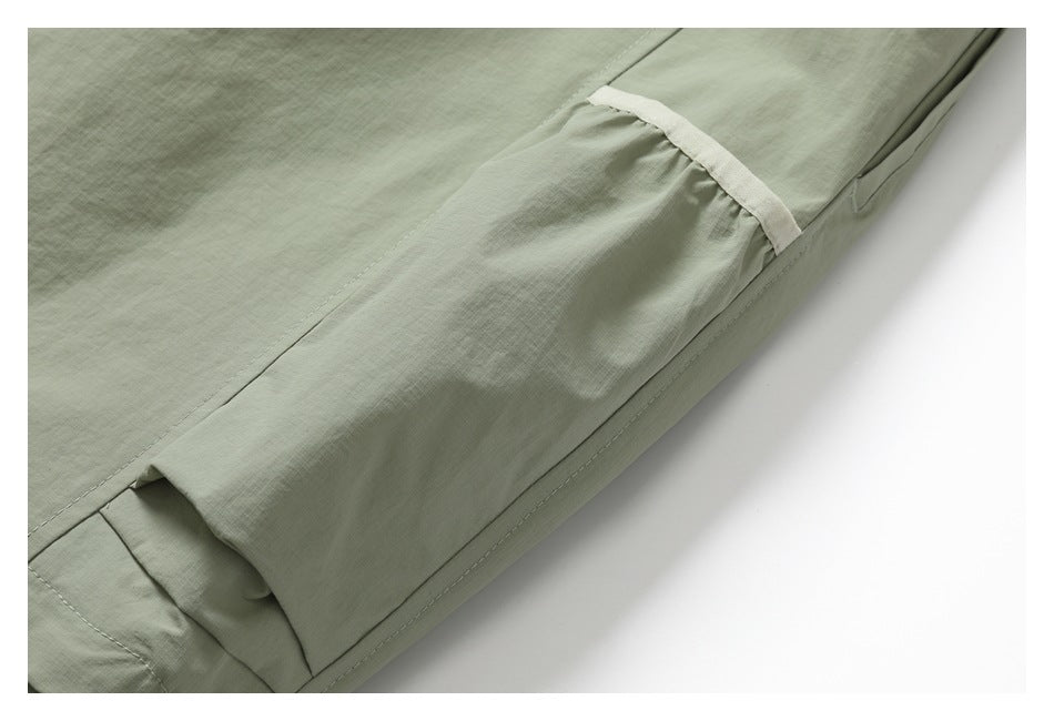Close-up of a gathered cargo pocket with a pale trim strip on sage-green pants.