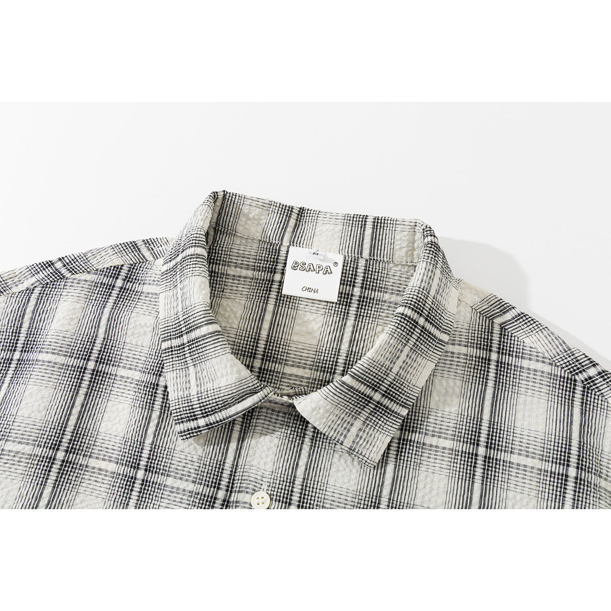 Close-up of a cream and black plaid shirt collar, button, and neck label.