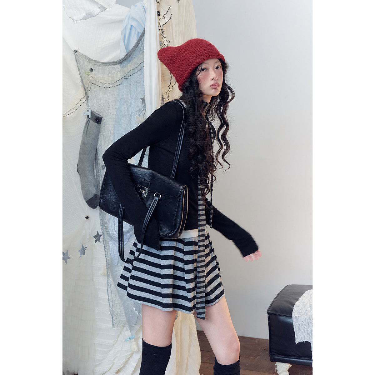 Model wearing a black top, black-and-gray striped skirt, red knit hat and knee-high socks.