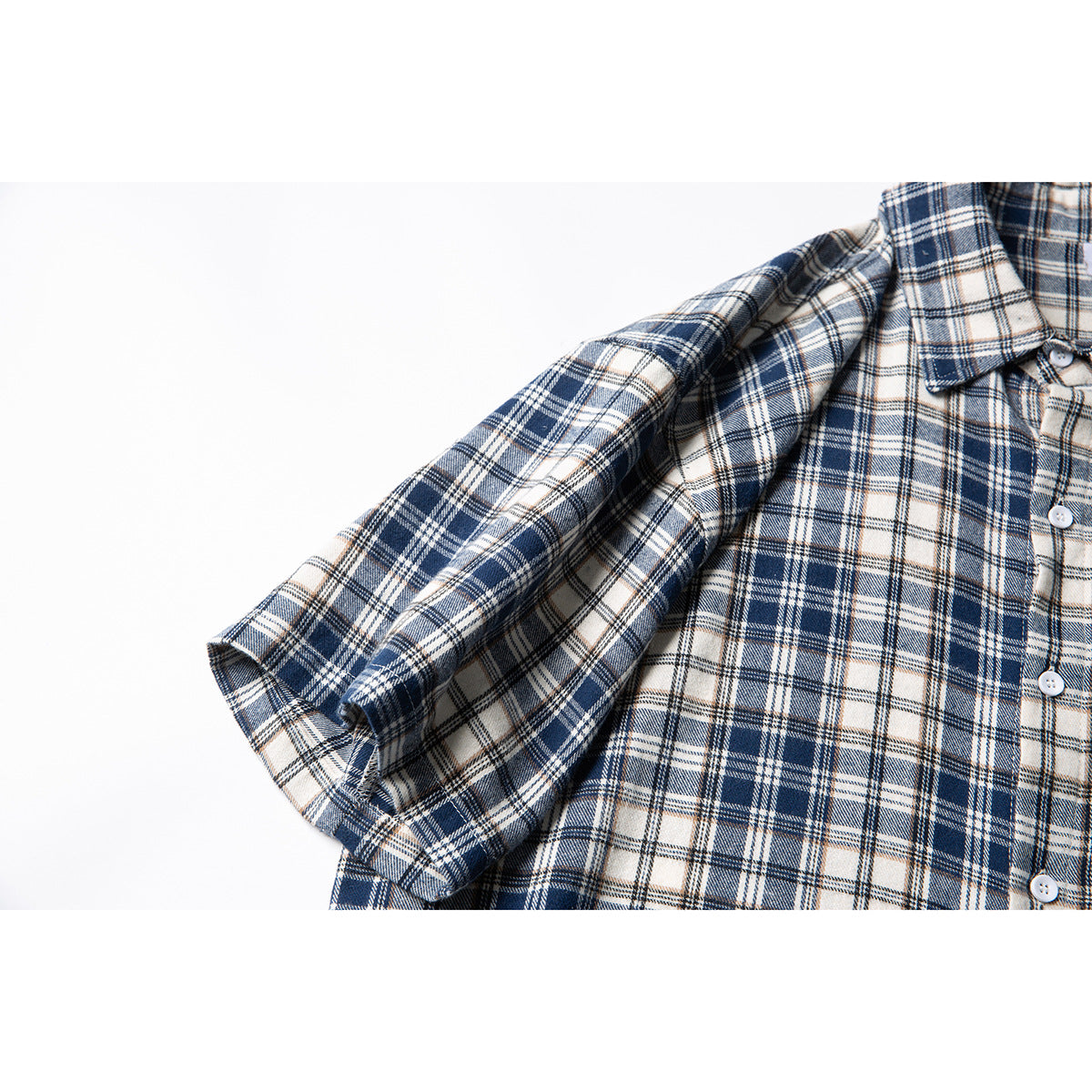 Close-up of the sleeve, cuff, and buttoned front of a navy, cream, and tan plaid shirt.