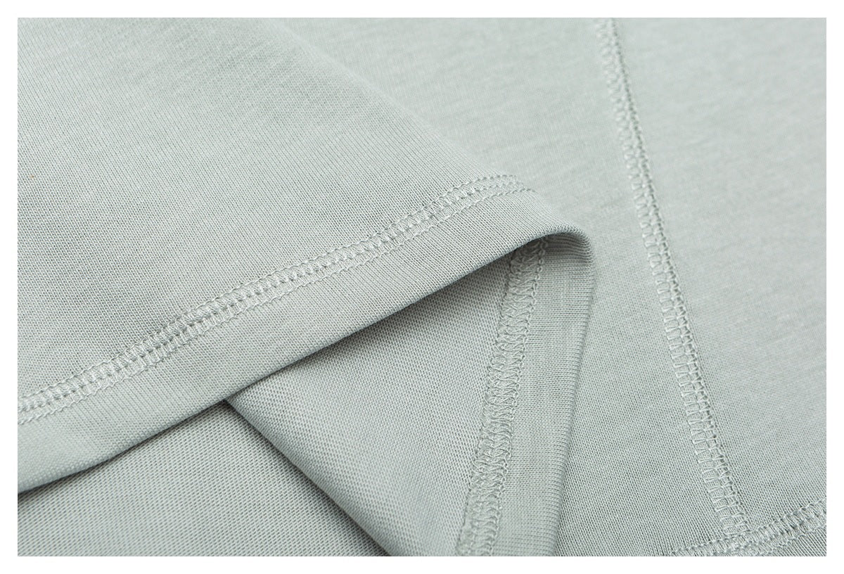 Close-up of a finished hem and overlocked seam on pale sage-gray knit fabric.