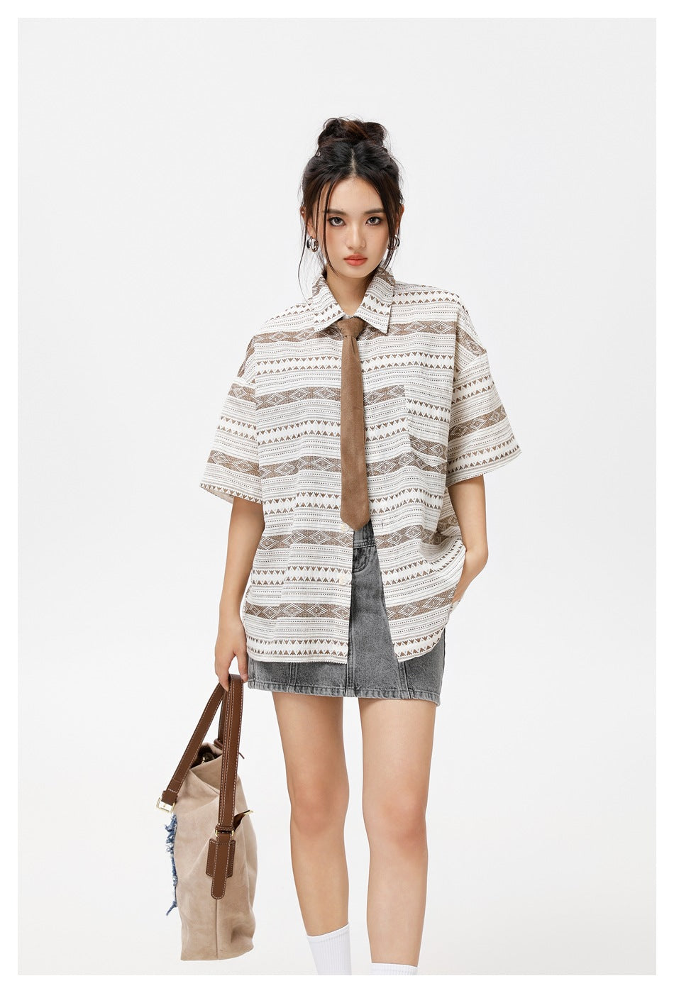 Closer view of a model wearing a taupe geometric short-sleeve shirt with a brown tie and gray denim mini skirt.