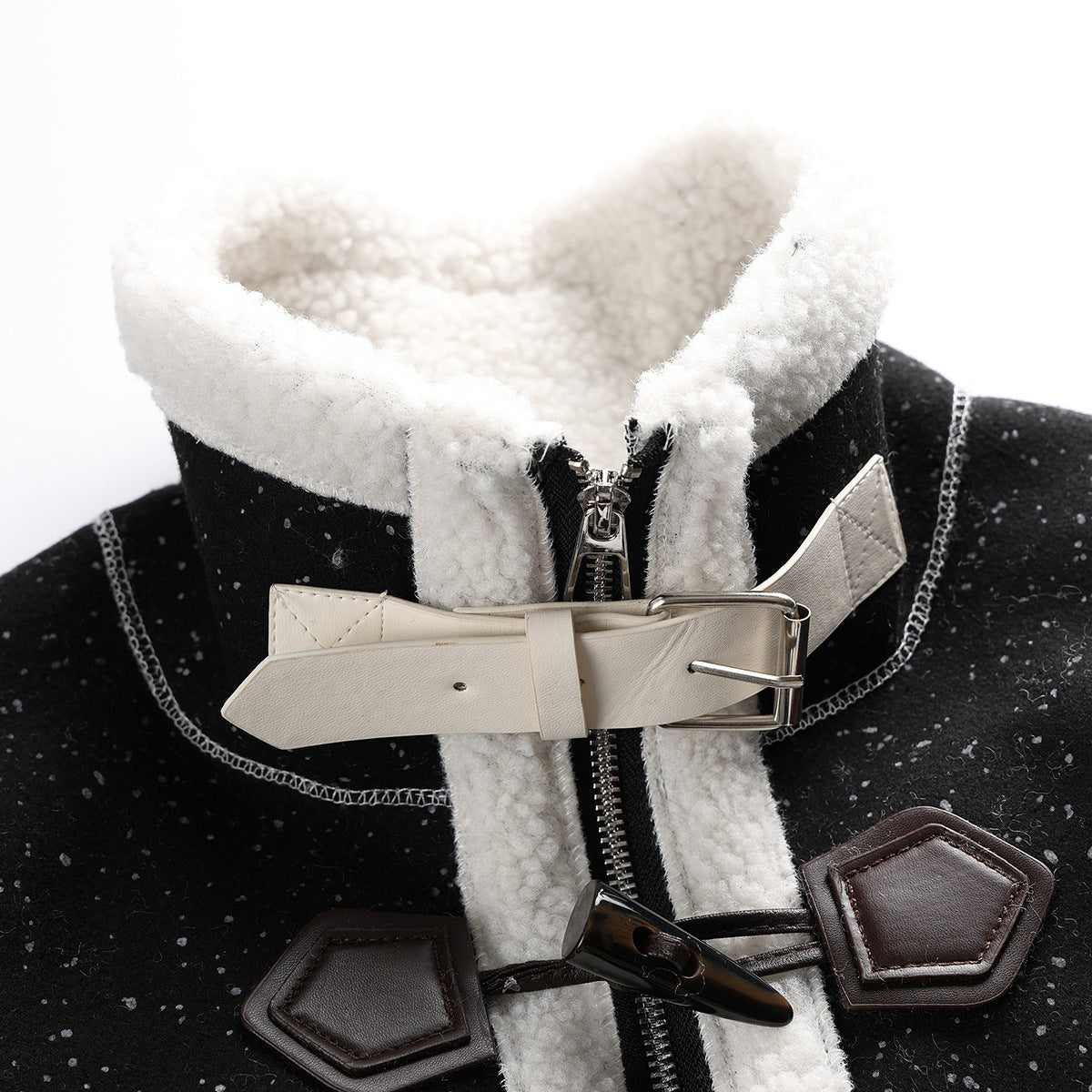 Close-up of a black flecked coat collar with cream fleece trim, front zipper, ivory buckle strap and dark toggle closures.