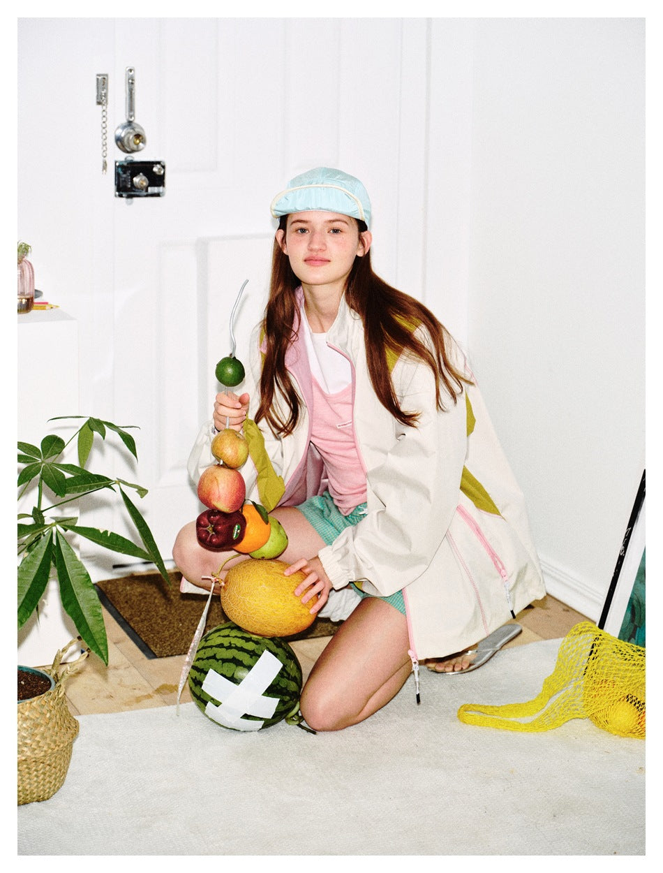Seated model wears an ivory jacket with pink and olive accents over a pink top and turquoise checked shorts.