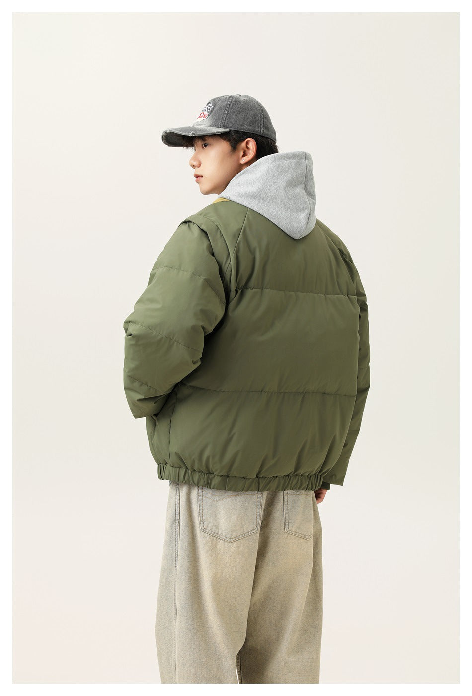 Rear view of a model wearing an olive-green padded jacket with horizontal seams and an elastic hem.