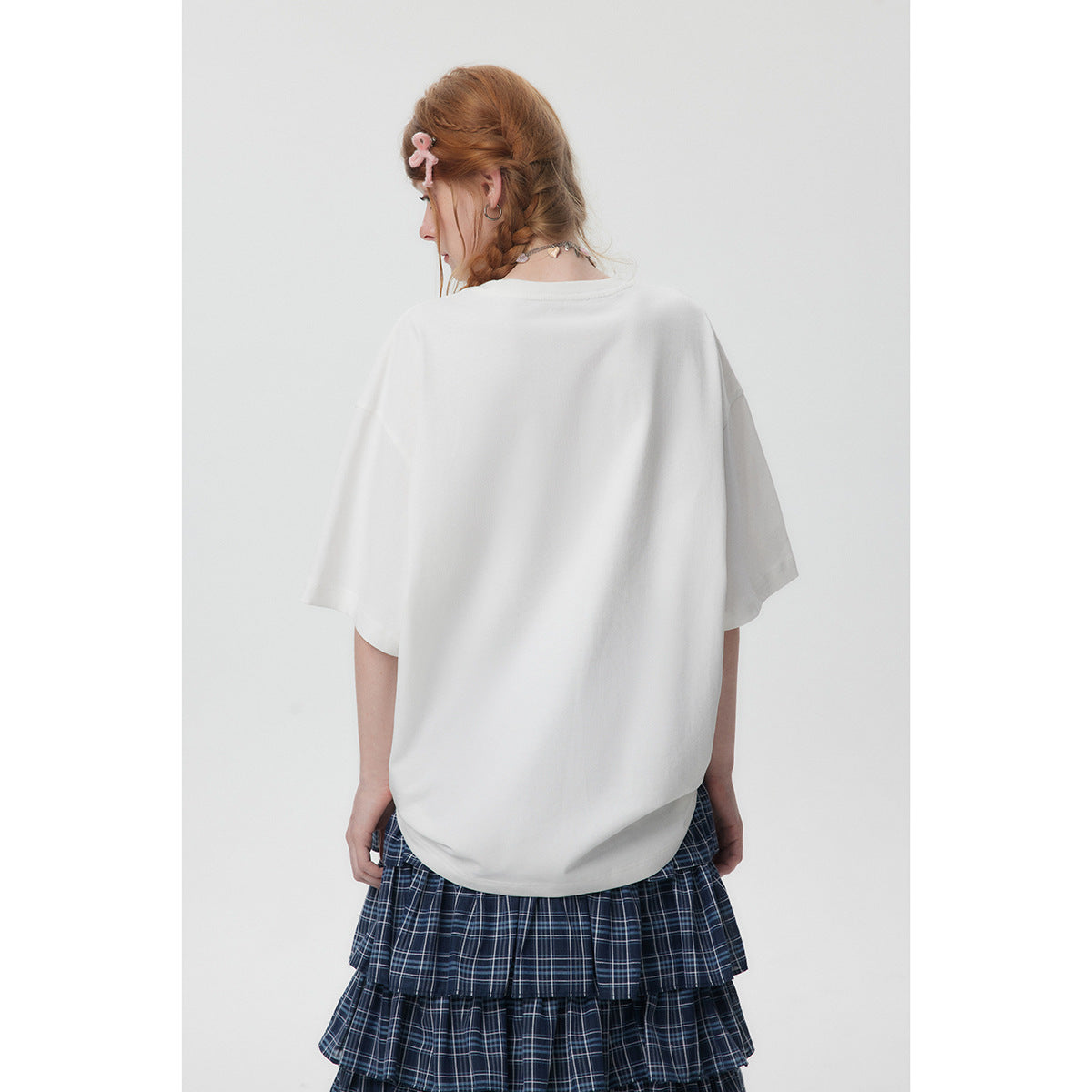Back view of a model in an oversized plain white T-shirt and navy plaid tiered skirt.