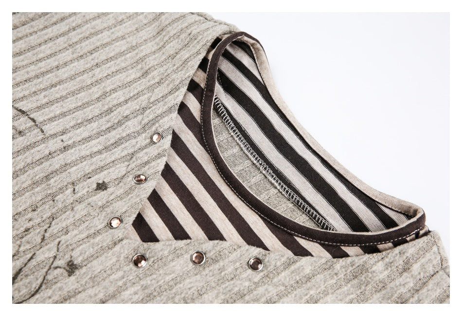 Close-up of a gray striped top's round neckline, dark striped inner facing, and metal studs.