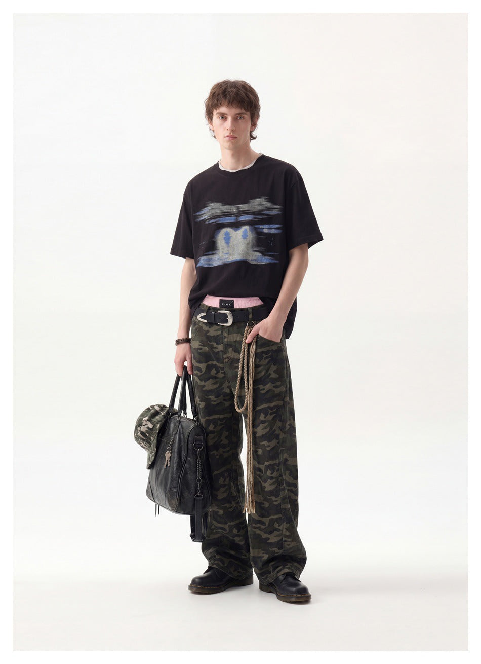 Full-length model wearing a black graphic T-shirt, loose camouflage trousers and black boots.