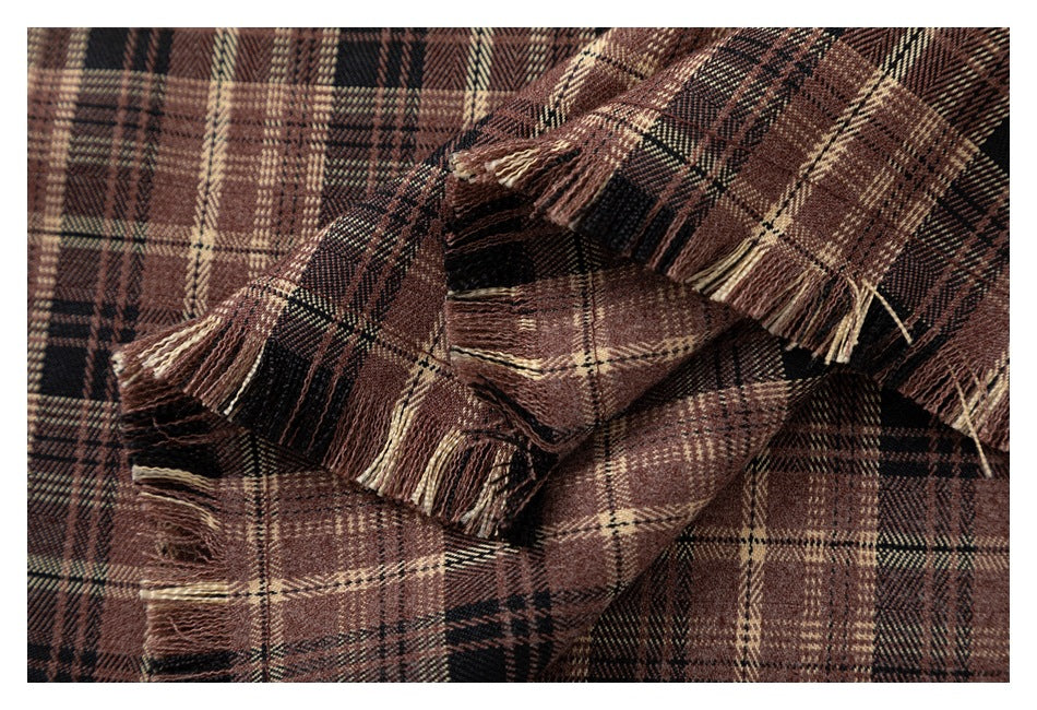Close-up of brown, black, and cream plaid fabric gathered in folds, with fringed edges.
