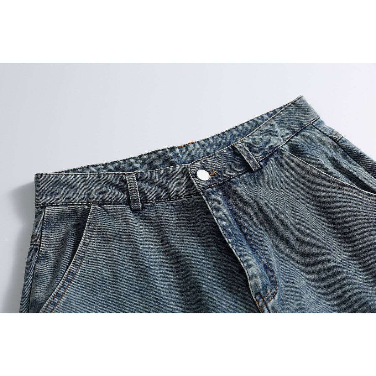 Close-up of blue-gray washed jeans showing the waistband, button, belt loops, fly, and front pocket edge.