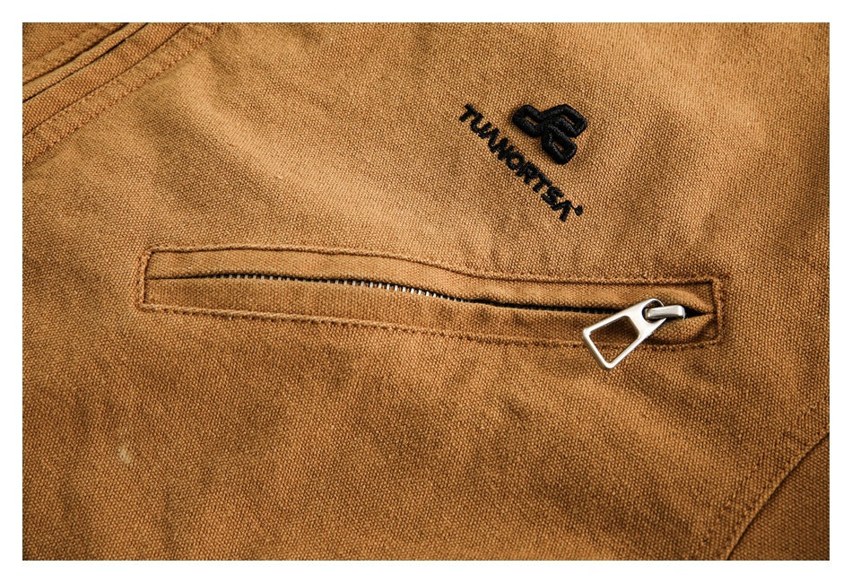 Close-up of a tan jacket's horizontal zip pocket and embroidered logo.