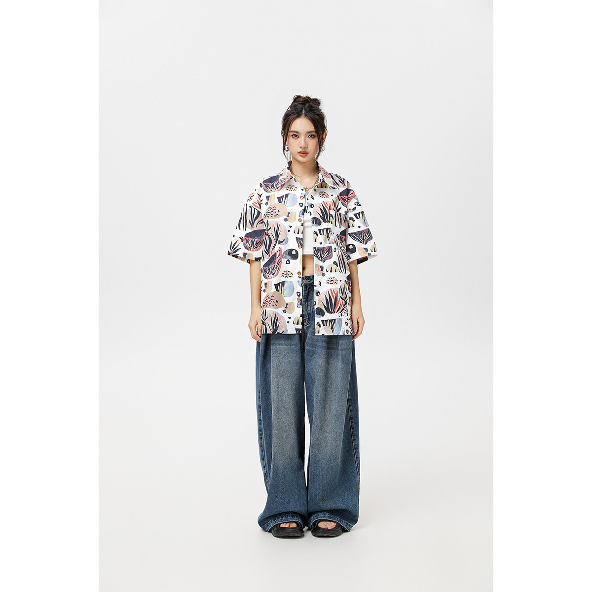 Front view of a model wearing a white abstract botanical-print short-sleeve shirt open over a white top, with wide-leg jeans.