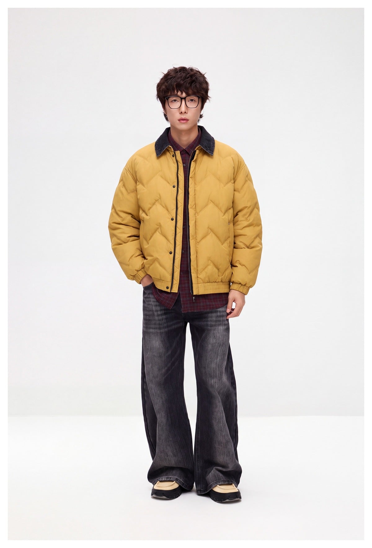 Man wearing a yellow quilted jacket over a plaid shirt with wide-leg dark washed jeans, full-length view