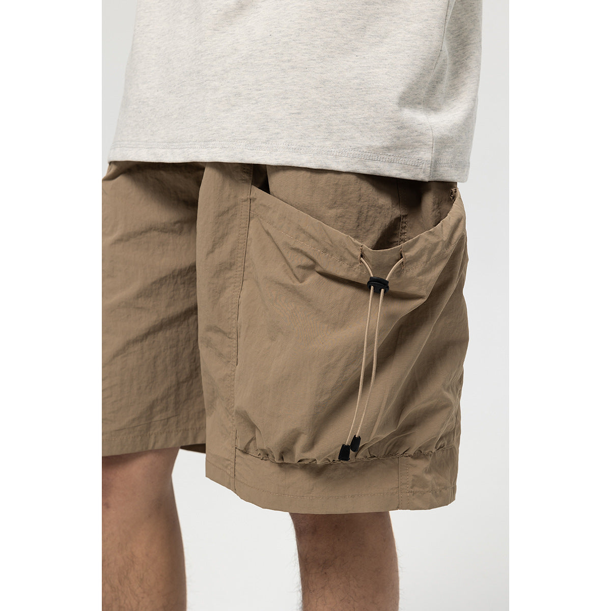Close crop of a model wearing taupe cargo shorts with a large drawcord-adjustable side pocket.