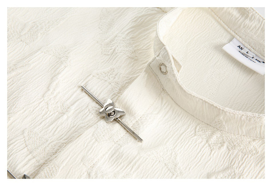 Close-up of the ivory garment's collar, eyelet and silver flower-shaped fastener.
