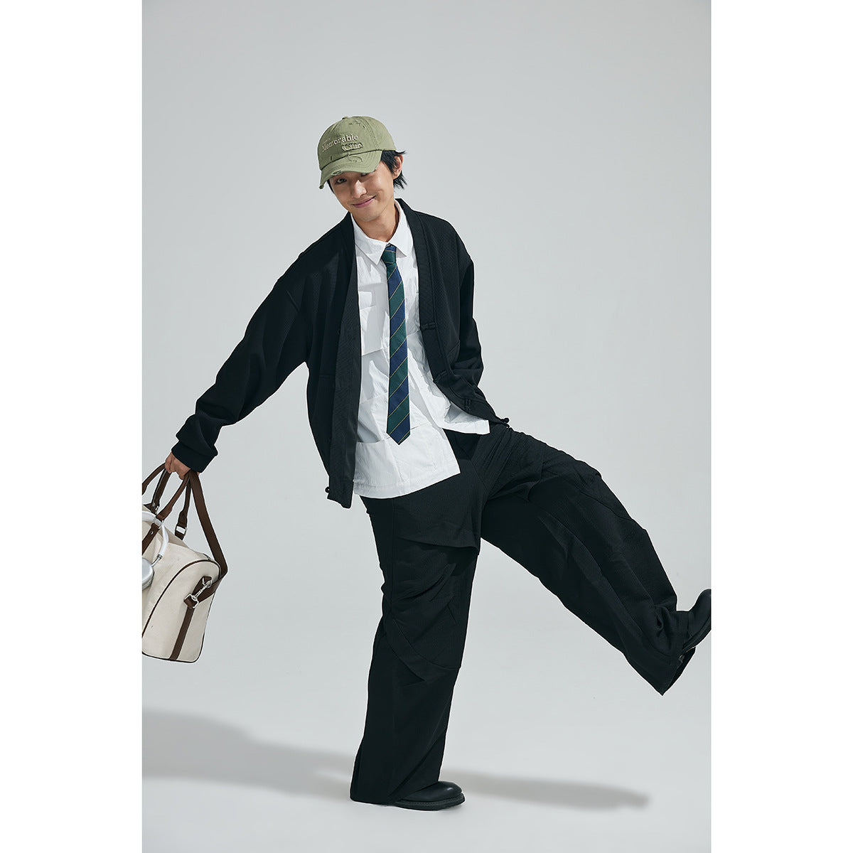 Model wearing a black cardigan and wide-leg trousers with a white shirt and striped tie, posing with one leg raised.