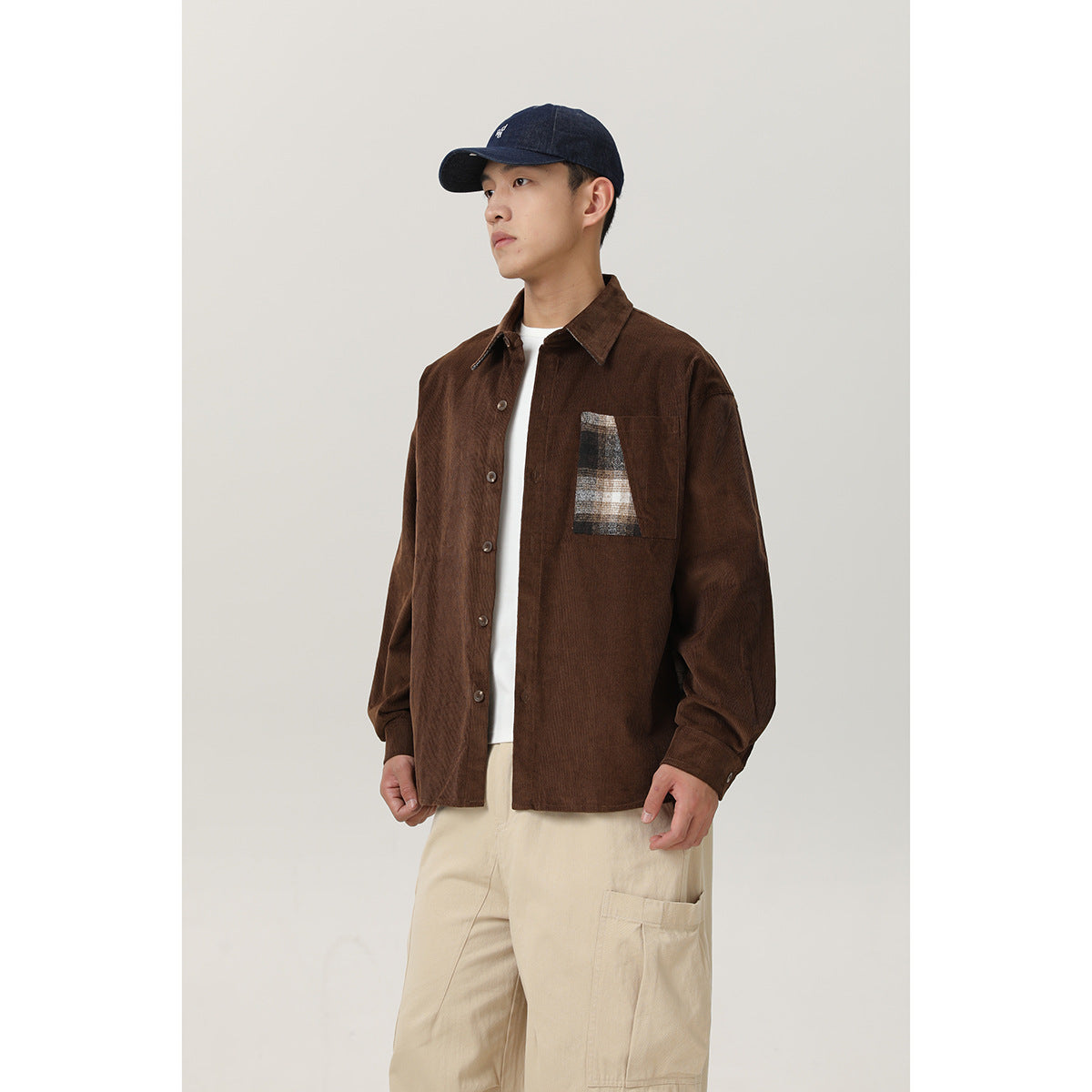 Model wearing a brown button-front shirt with a plaid chest pocket, cream cargo pants, and a navy cap.