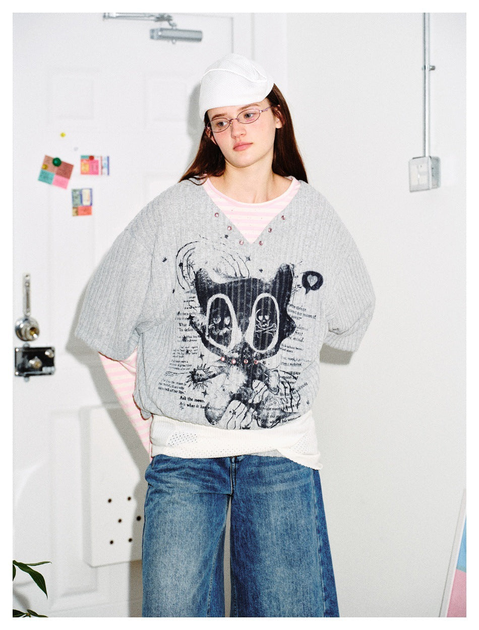Model wearing the gray ribbed layered top with cat graphic over a pink striped tee, with wide-leg jeans and a white cap