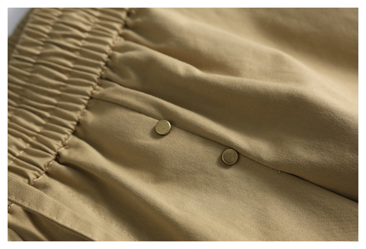 Close-up of tan shorts showing the elastic waistband and two gold-tone buttons at the waist.